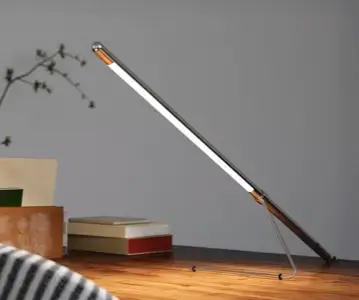Moderne Tischlampe auf einem Holztisch mit Bücherstapeln im Hintergrund.