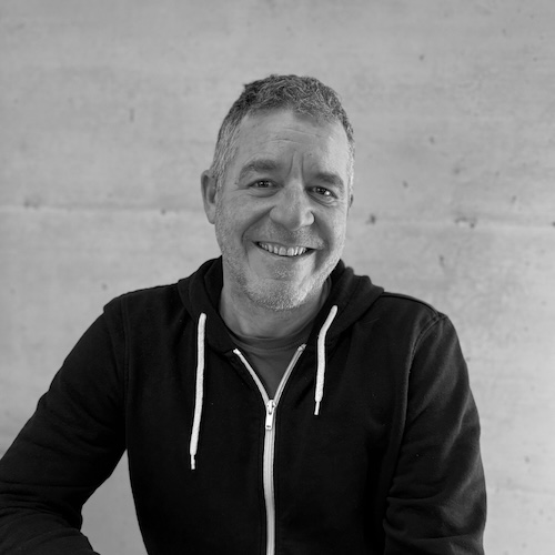 The smiling designer Beat Seiler in a black hoodie in front of a concrete wall. He is the designer of the BTX lamp model by Belux.