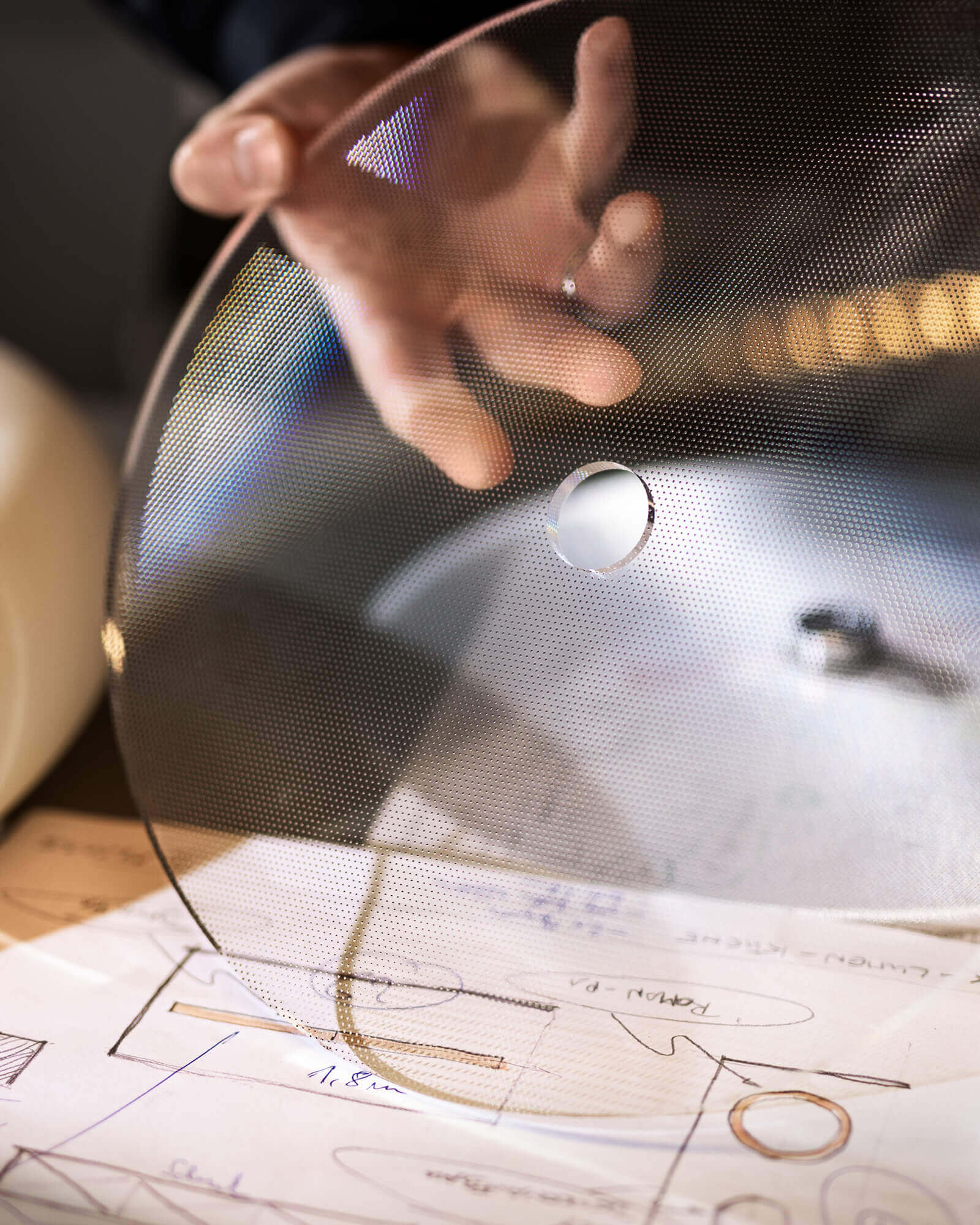 Designer hält perforierte Materialien über technischen Zeichnungen.