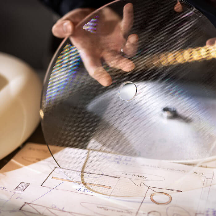 Designer hält perforierte Materialien über technischen Zeichnungen.