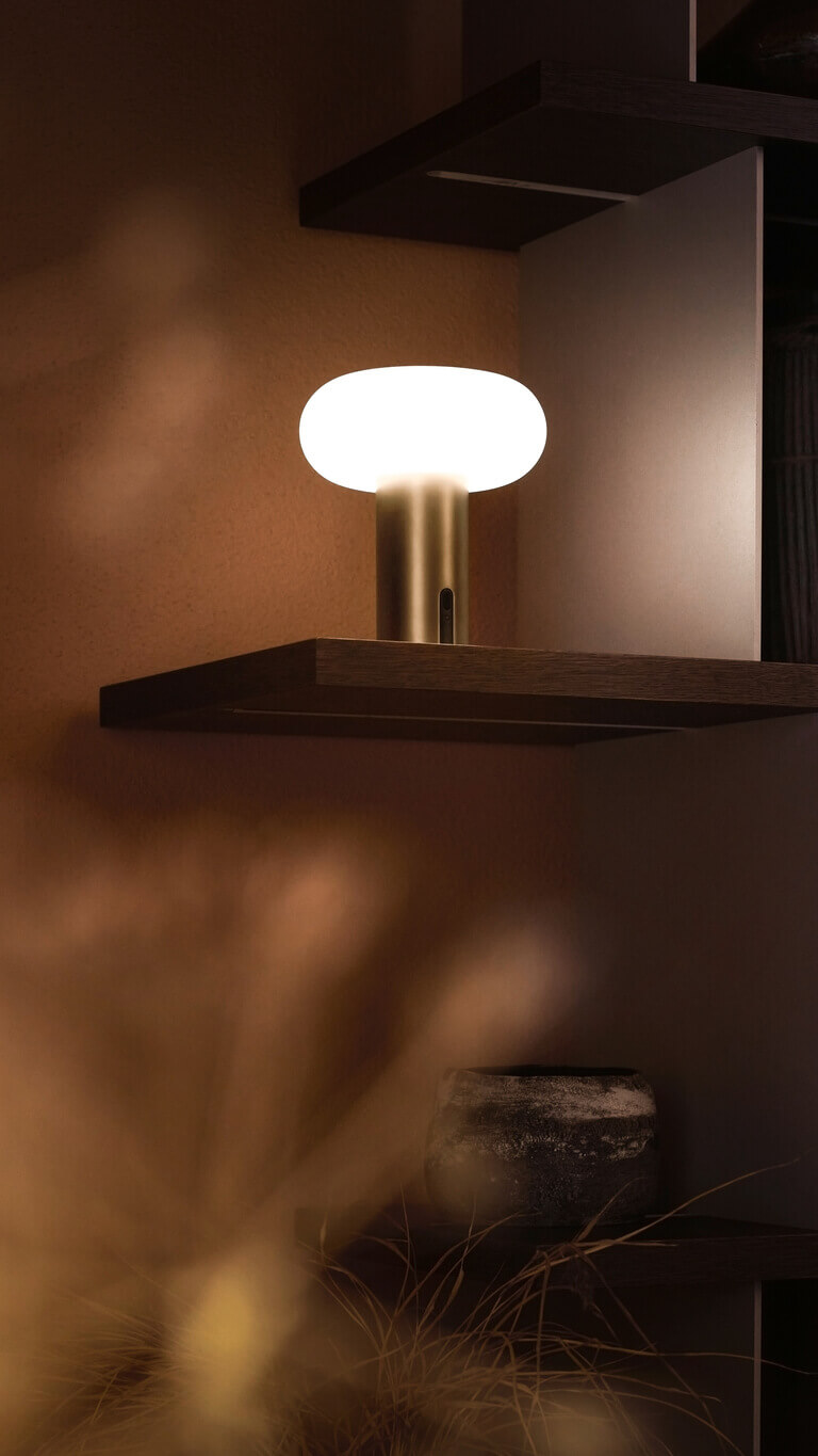 Belux „Oto Portable“ leuchtet in einer Regalnische; dunkle Keramikobjekte stehen daneben.
