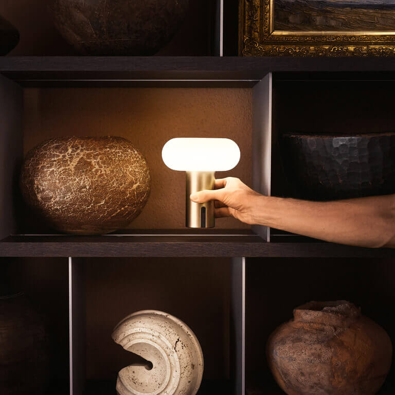 Hand places a glowing Belux "Oto Portable" on a shelf between decorative vessels.