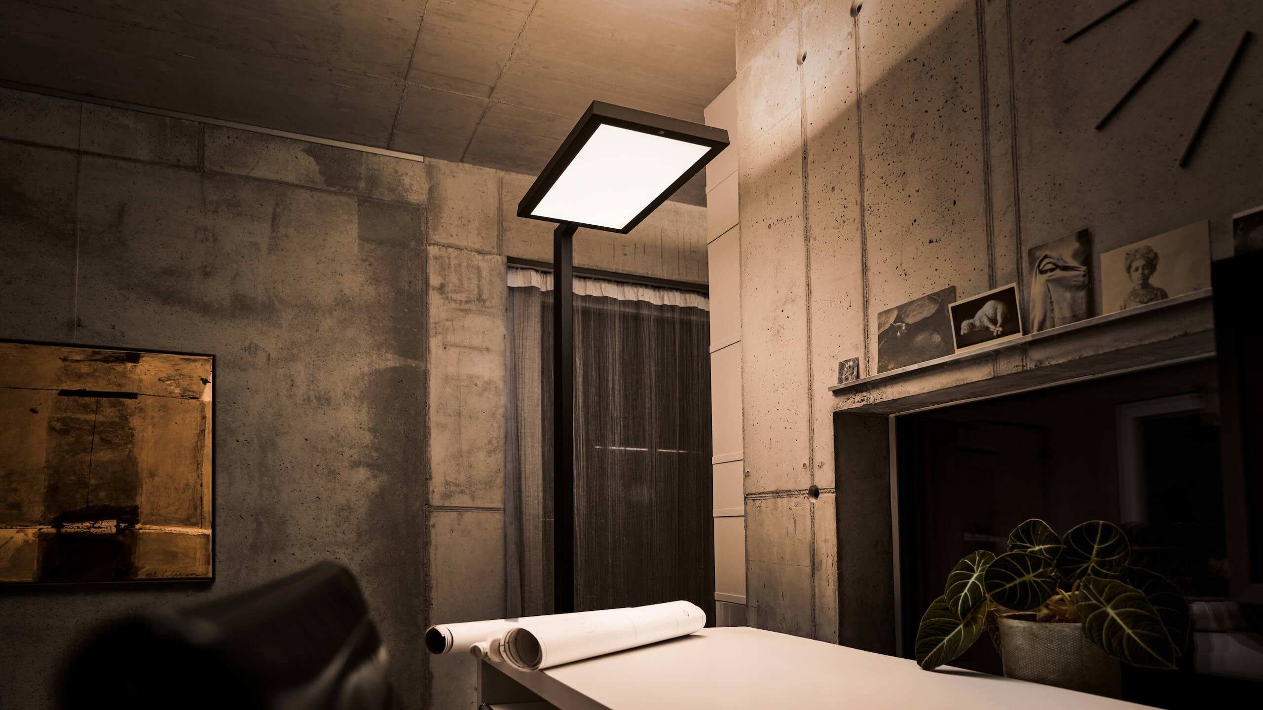 Belux-Stehleuchte „Bob“ mit großem, rechteckigem Leuchtpanel neben Tisch mit gerollten Plänen.