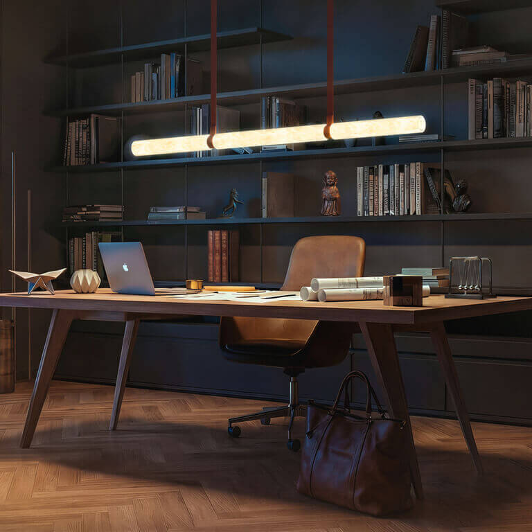 Lineare Pendelleuchte Belux „Equinox“ leuchtet über einem Schreibtisch mit Laptop vor einer dunklen Bücherwand.