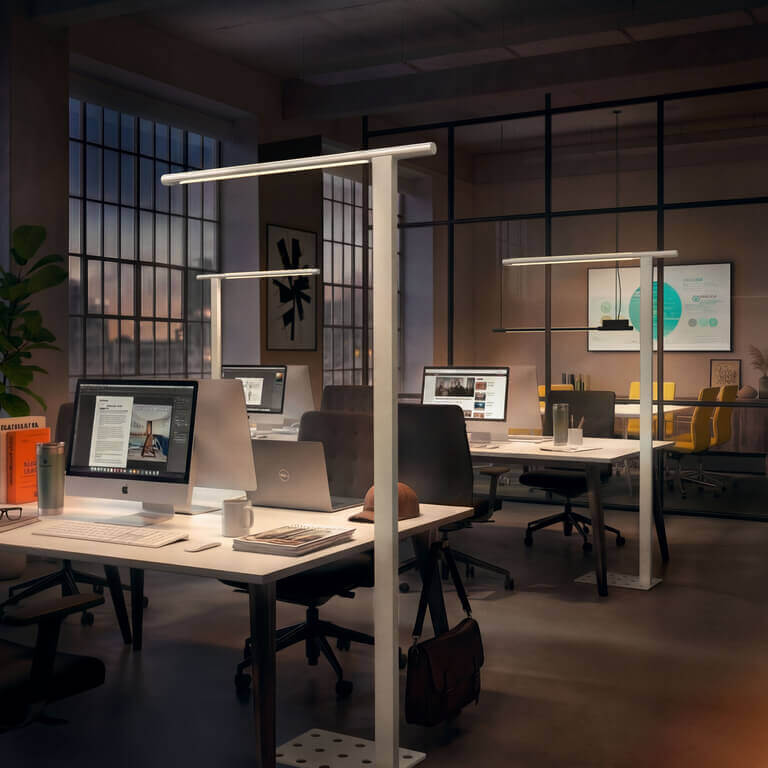 Modernes Großraumbüro mit mehreren Schreibtischen; mehrere schlanke Belux-Stehleuchten „Mono“ mit horizontalem Leuchtenkopf beleuchten die Arbeitsplätze.