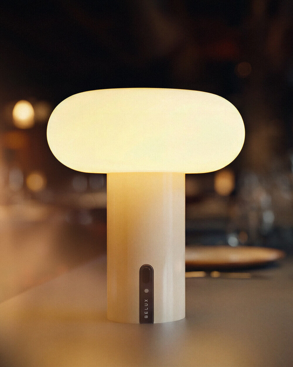 Nahaufnahme der Belux „Oto Portable“ mit ovalem, hell leuchtendem Schirm auf zylindrischem Fuß.