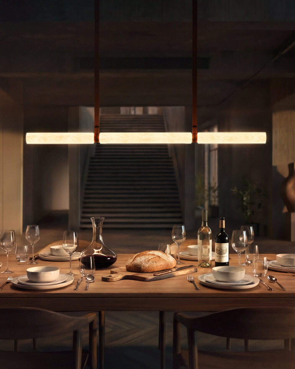 Gedeckter Esstisch mit Brot, Wein und Gläsern; darüber hängt die lineare Pendelleuchte Belux „Equinox“ und leuchtet warm.