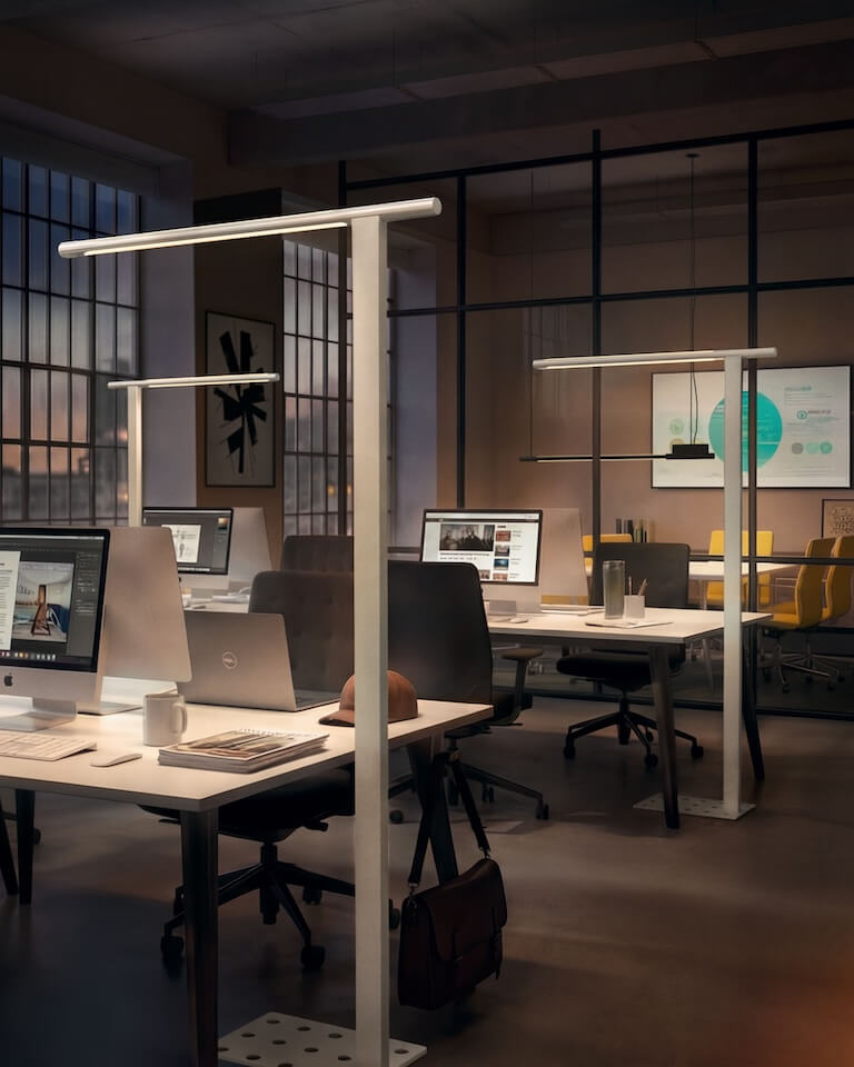Modernes Großraumbüro mit mehreren Schreibtischen; mehrere schlanke Belux-Stehleuchten „Mono“ mit horizontalem Leuchtenkopf beleuchten die Arbeitsplätze.