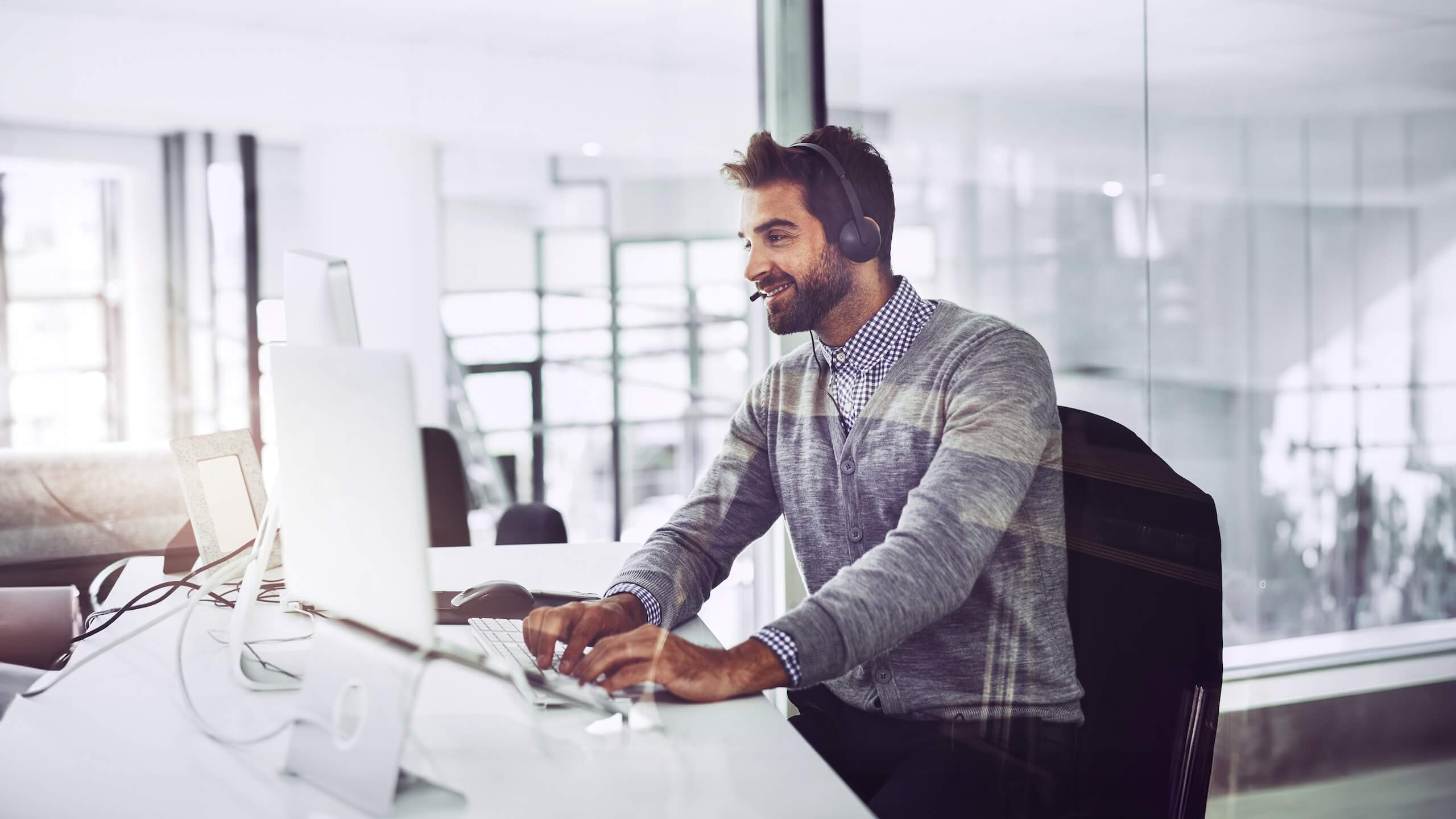 Mitarbeiter mit Headset sitzt am Schreibtisch und arbeitet am Computer in einem hellen Büro.