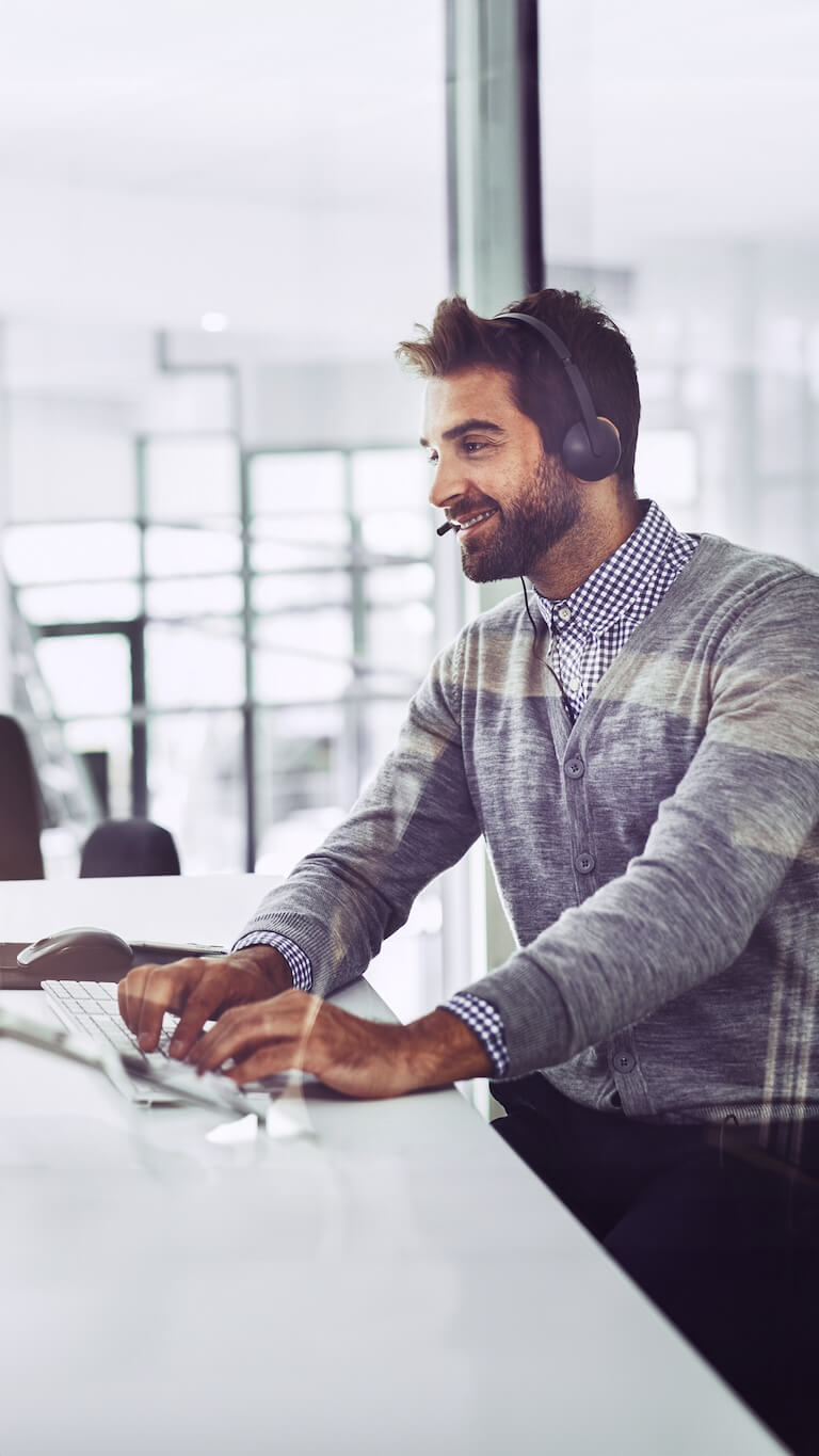Mitarbeiter mit Headset sitzt am Schreibtisch und arbeitet am Computer in einem hellen Büro.