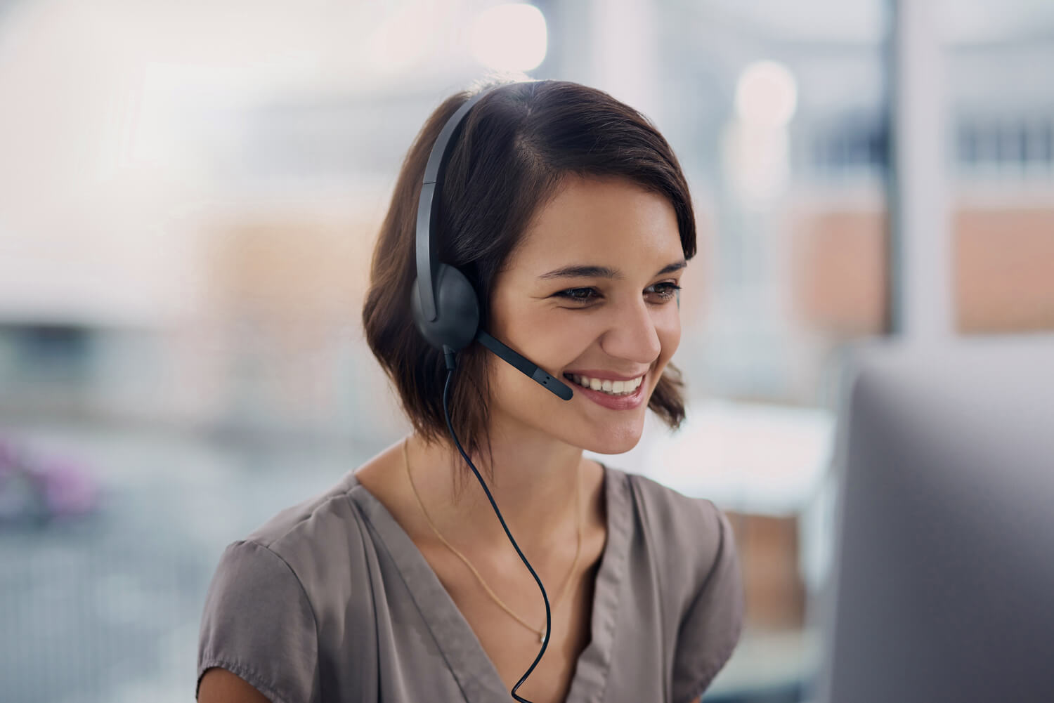 Smiling employee wearing a headset in a bright office, looking at a screen.