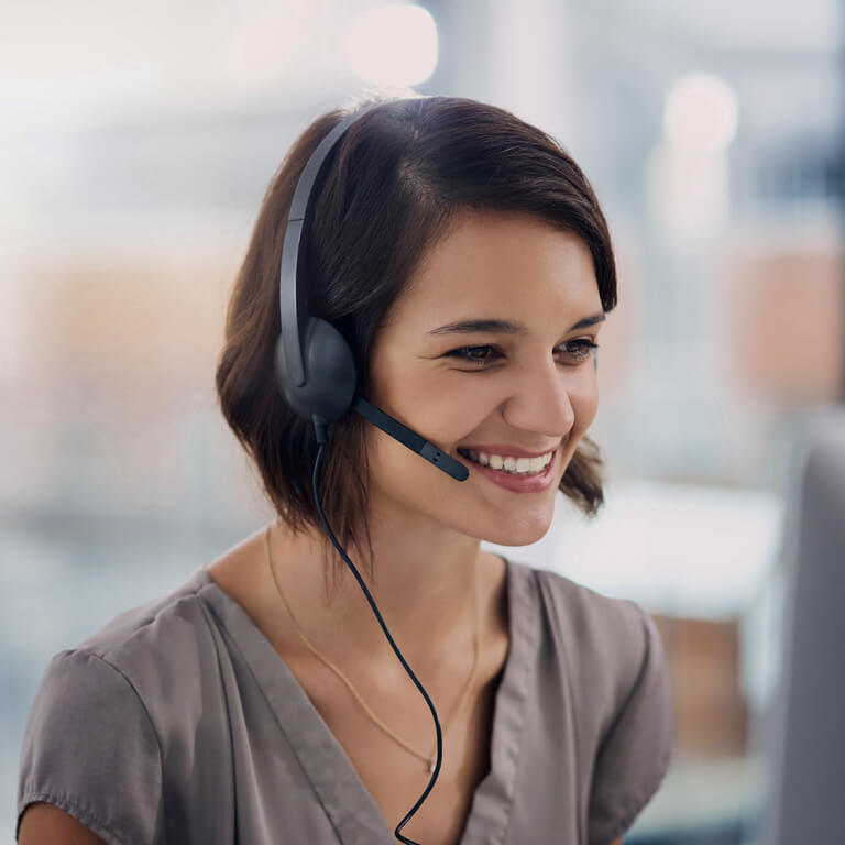 Smiling employee wearing a headset in a bright office, looking at a screen.